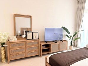 Une chambre d’hôtel avec une commode en bois, un téléviseur à écran plat, un lit et un grand miroir.