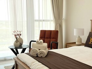 A hotel room with a bed, a chair, a small table with a vase, and a lamp. - Modern Studio in Dubai - Pool, Gym & Parking (Dubai)