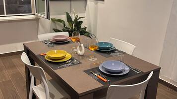 Un comedor con una mesa dispuesta para dos personas, sillas blancas y una planta en maceta.