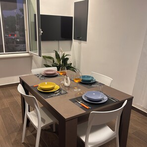 A dining area with a table set for two, white chairs, and a potted plant. - Casa Surace, Apartment 1 (Reggio Calabria)