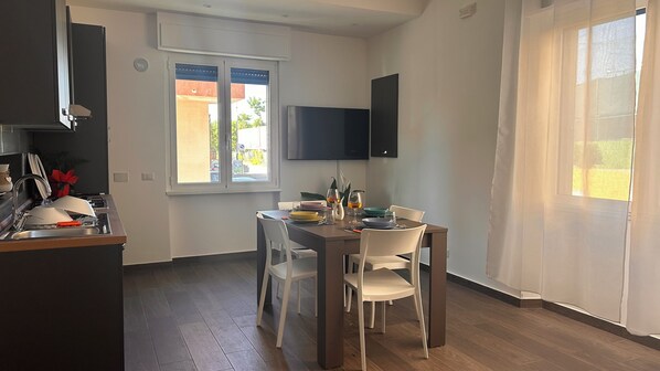 A modern kitchen with a dining area, a flat-screen TV mounted on the wall, and a window with a view of the outside. - Casa Surace, Apartment 1 (Reggio Calabria)