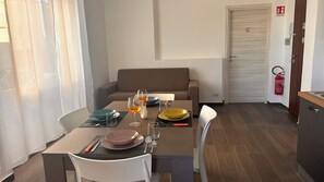 A dining area with a table set for two, a sofa, and a fire extinguisher. - Casa Surace, Apartment 1 (Reggio Calabria)