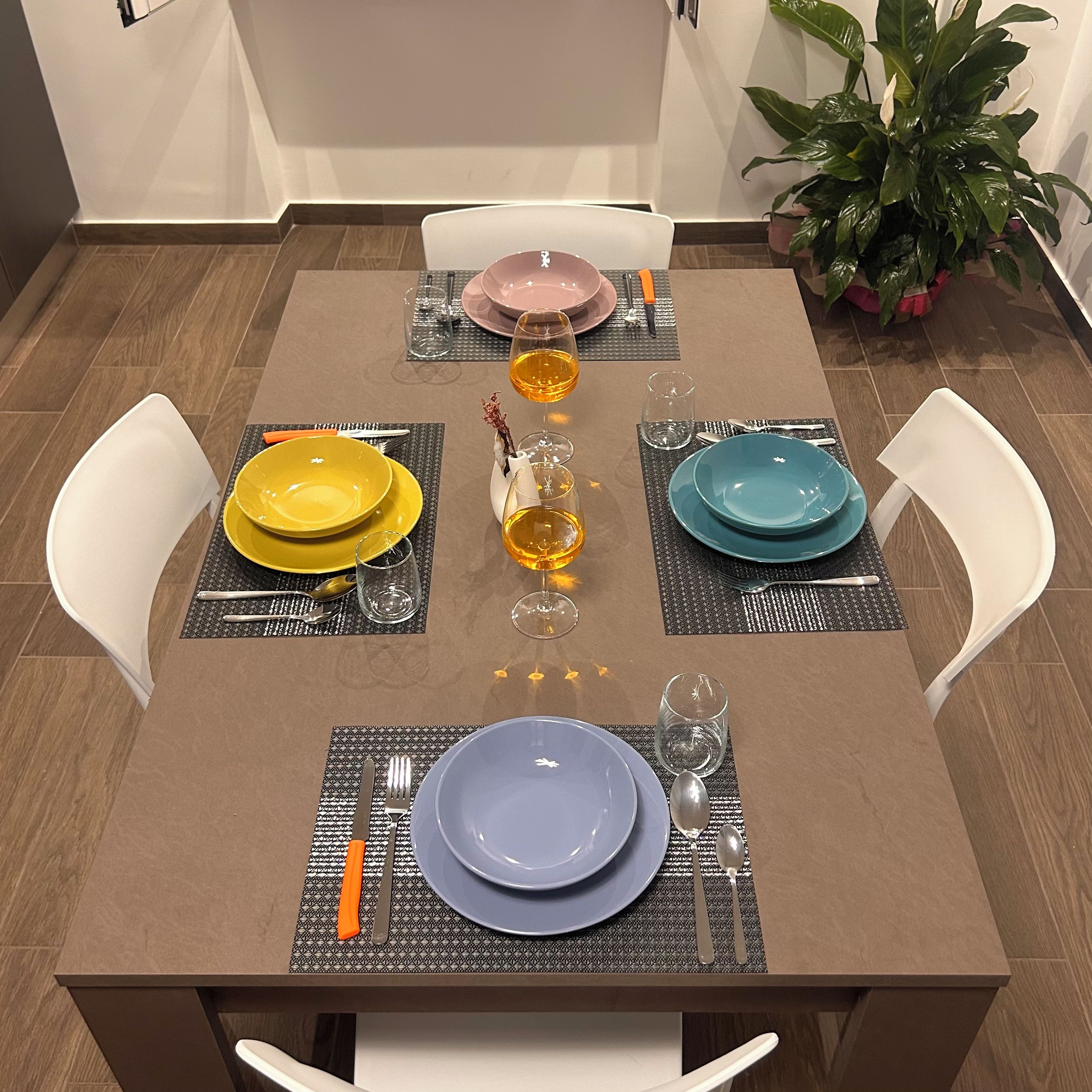 Una mesa de comedor lista con platos, cubiertos y vasos, rodeada de sillas.