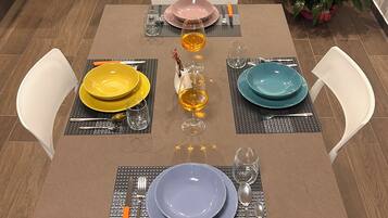 Una mesa de comedor lista con platos, cubiertos y vasos, rodeada de sillas.
