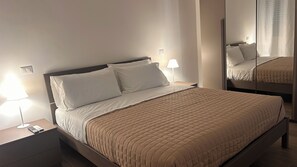 A neatly made bed with a quilted cover, two bedside lamps, and a bedside table with a remote control. - Casa Surace, Apartment 1 (Reggio Calabria)