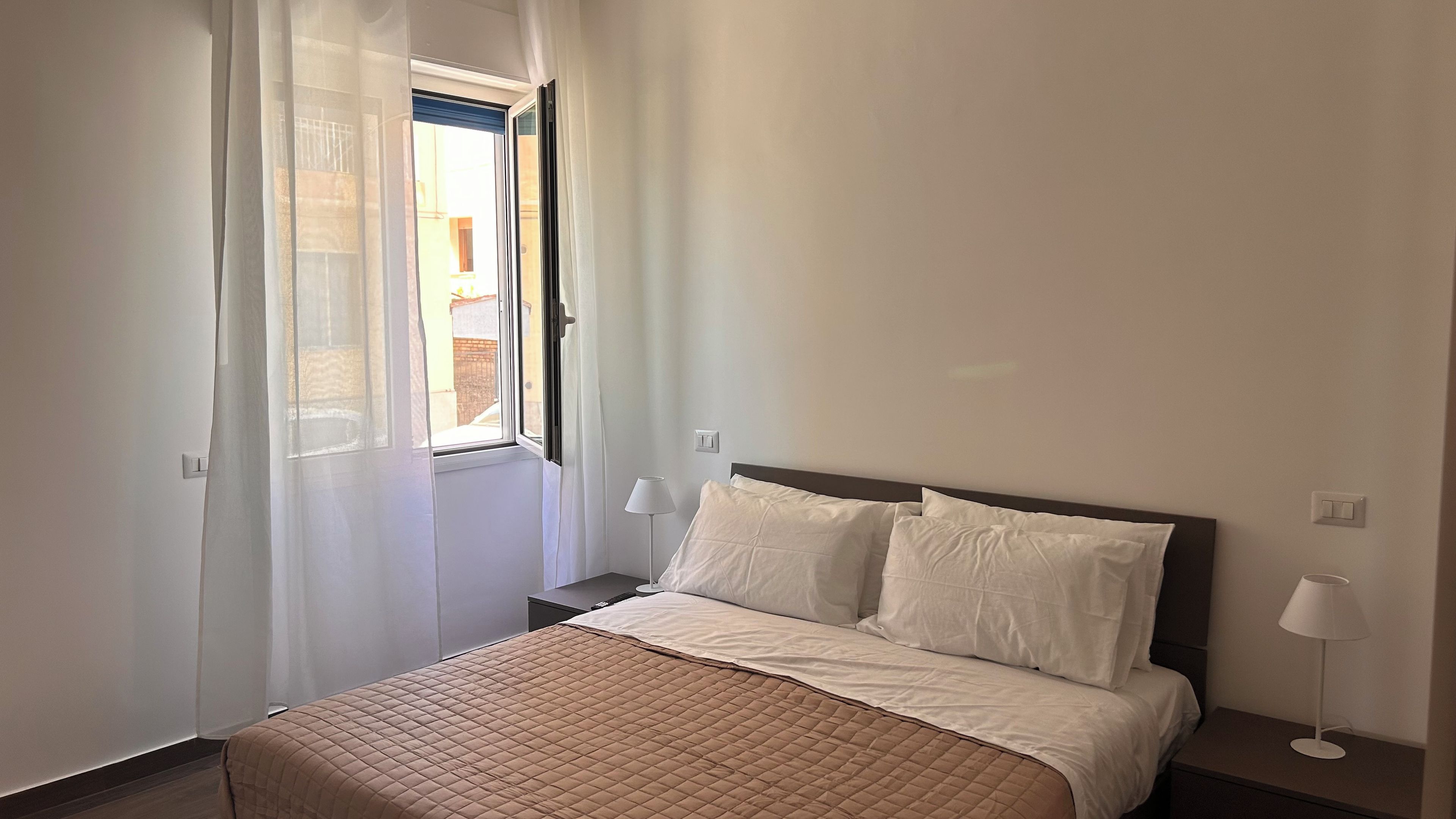 Un dormitorio con cama, mesita de noche, lámpara y ventana con cortinas.