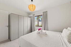 Ein Schlafzimmer mit einem Bett, einem Kleiderschrank, einem Fenster mit Vorhängen und einer Klimaanlage.