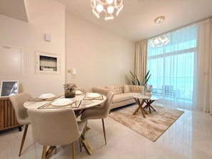 A modern living room with a dining area, large windows, and a view of the city. - Stylish 1BR Apartment - Skyz by Danube - Arjan (Dubai)