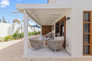 A covered outdoor seating area with wicker furniture and a view of the street. - J&M Trupial | Stylish Caribbean Stay in Vredenberg (Willemstad)