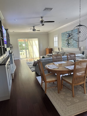 A spacious living area with a dining table, chairs, a sofa, and a television mounted on the wall. - Charming 3-bedroom house in Sarasota on a quiet street, 1/2 mile out of town. (Sarasota)