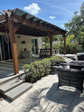 An outdoor patio area with a pergola, wicker furniture, and a view of a house. - Charming 3-bedroom house in Sarasota on a quiet street, 1/2 mile out of town. (Sarasota)