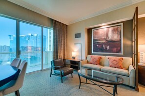 Ein Hotelzimmer mit großem Fenster, einer Couch, einem Sessel, einem Couchtisch und einem Gemälde an der Wand.