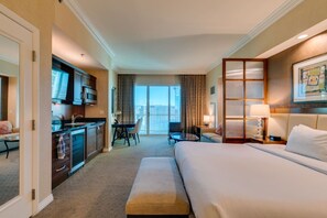 Quarto de hotel com cama, escrivaninha com cadeira, televisão e vista para a cidade pela janela.