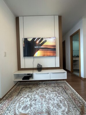 A modern living room with a flat-screen TV mounted on a wall, a white entertainment unit below, and a patterned rug on the floor.