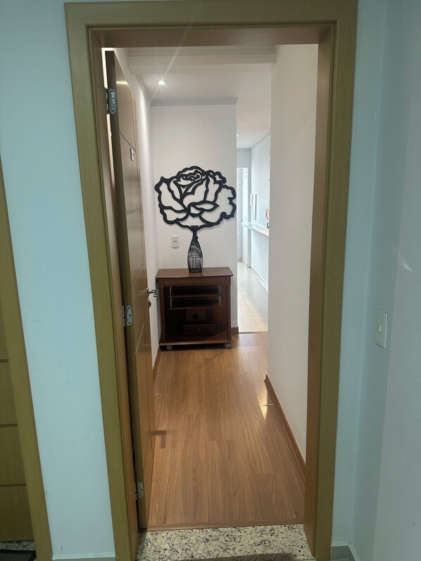 A hallway with a wooden floor, a wall-mounted decorative piece, and a small wooden cabinet.
