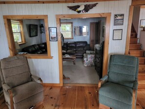 A cozy living room with a wooden floor, two armchairs, a leather sofa, and a staircase leading upstairs. - Pet friendly Lakefront Cottage with 4 Bedrooms and plenty of amenities! (Hartland)
