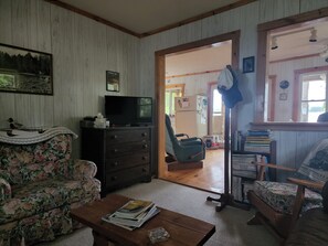 Un salon avec un téléviseur posé sur une commode, un canapé à motifs floraux, une table basse en bois et une bibliothèque.