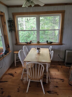 A wooden-paneled room with a large window, a table with chairs, and a ceiling fan.