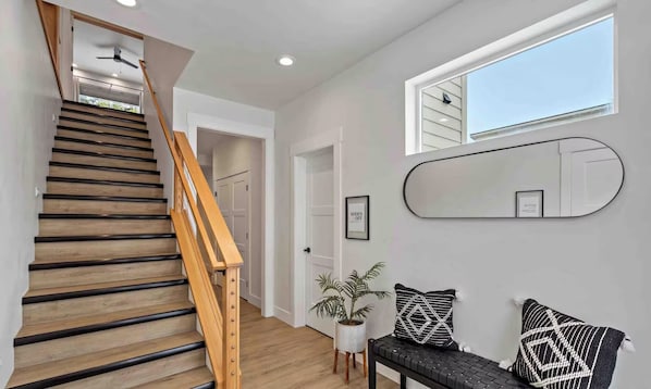 A staircase with wooden steps and a wooden handrail, leading to a hallway with white walls and a ceiling fan.