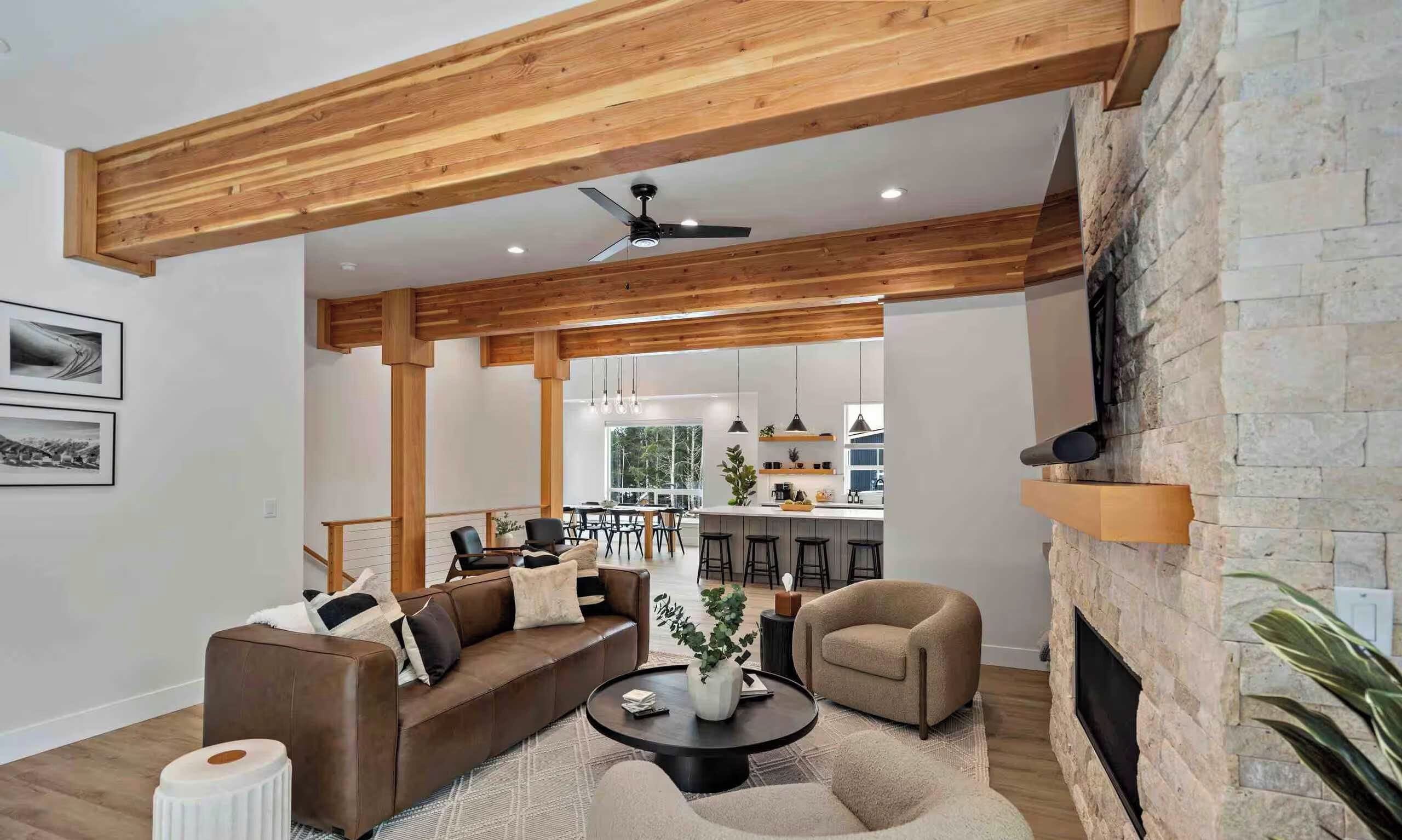 A modern living room with a stone fireplace, wooden ceiling beams, and a dining area with bar stools.
