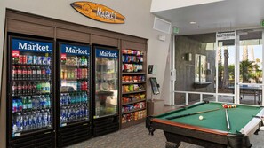 Une table de billard et des distributeurs automatiques portant l’inscription « The Market » se trouvent dans une pièce d’où l’on peut admirer des palmiers.
