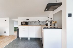 A modern kitchen with white cabinets, a black microwave, and a stainless steel sink. - Le Laon - Climatisation - Proche tram (Reims)