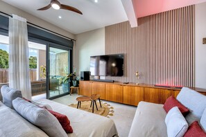 A modern living room with a large TV, wooden furniture, and a sliding glass door leading to a balcony. - Villa Romana - Piscine, jacuzzi - Tampon (Le Tampon)