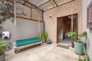 Un espacio al aire libre acogedor con una hamaca, plantas en macetas y un muro de piedra.