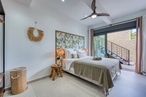 A bedroom with a bed, a ceiling fan, a wall-mounted light, a woven basket, and a view of the outside. - Villa Romana - Piscine, jacuzzi - Tampon (Le Tampon)