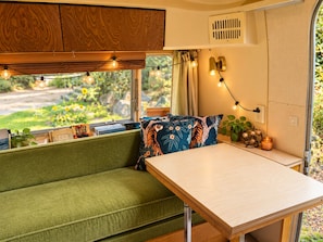 A cozy interior with a green sofa, a wooden table, and string lights. - Vintage Airstream Caravel Retreat Near Beach & Sea-Tac (Des Moines)