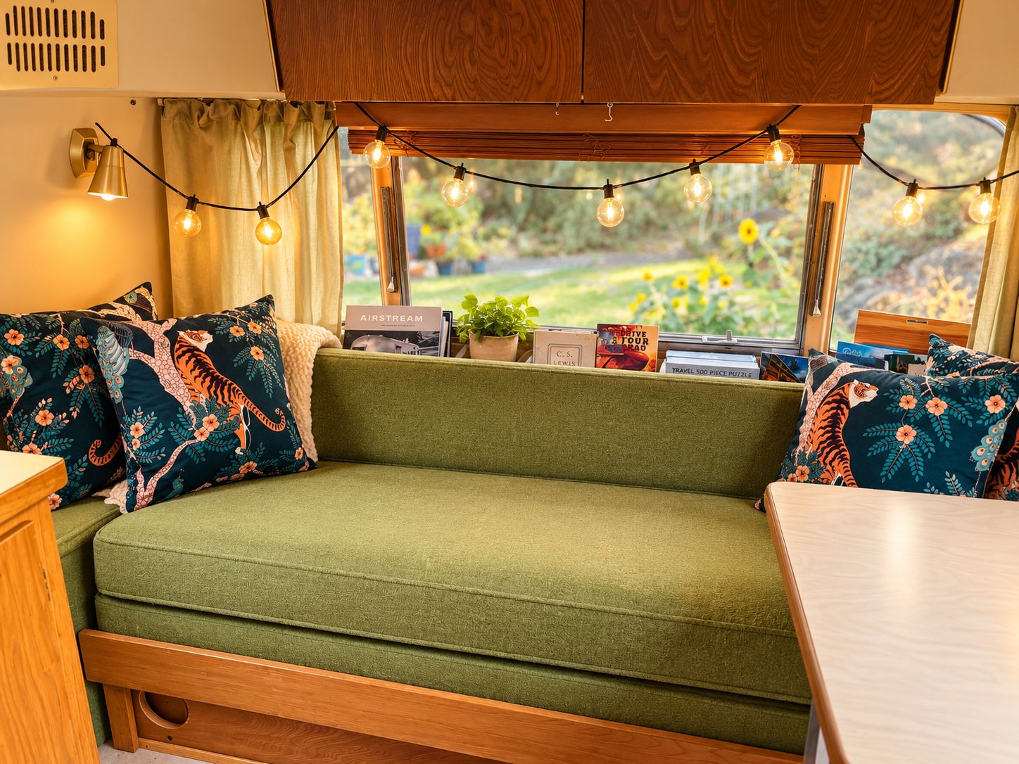A cozy interior with a green sofa, patterned pillows, a wooden table, and string lights.
