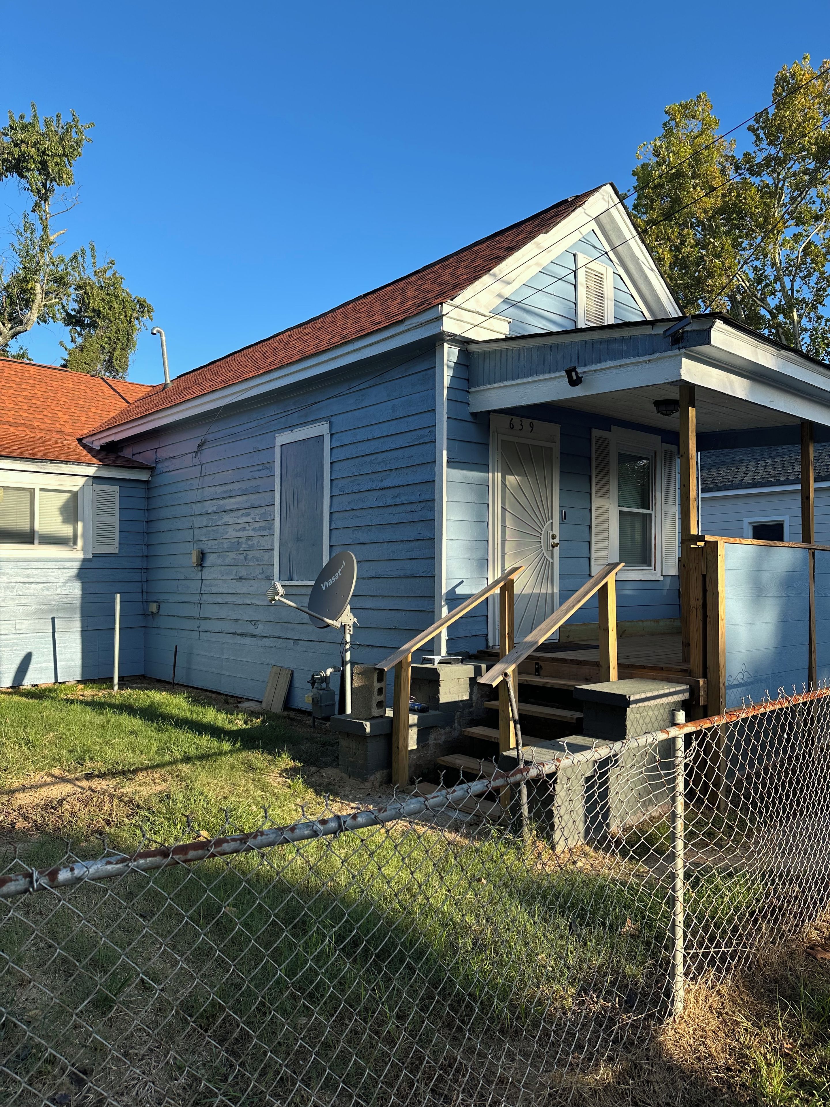A single-story house with a porch, a satellite dish, and a fenced yard.