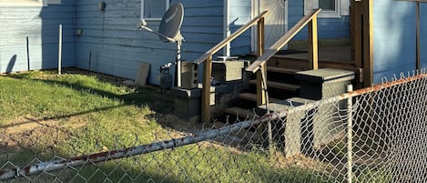 A single-story house with a porch, a satellite dish, and a fenced yard.