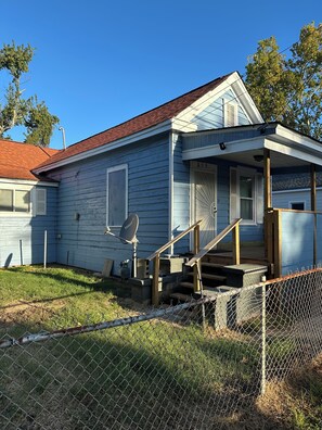 Ein eingeschossiges Haus mit Veranda, Satellitenschüssel und umzäunter Garten.