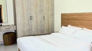 A bedroom with a bed, a wardrobe, a round ottoman, and a mirror.