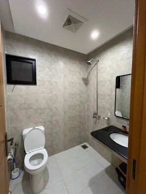 A modern bathroom with a toilet, shower, sink, and a mounted television. - Tranquil 1-bedroom apartment with AC in lively Lahore (Lahore)