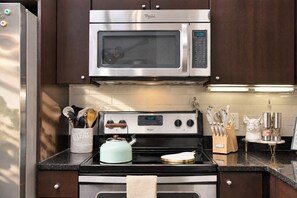 Une cuisine équipée d’un four à micro-ondes Whirlpool en acier inoxydable, d’une cuisinière et d’une hotte aspirante.