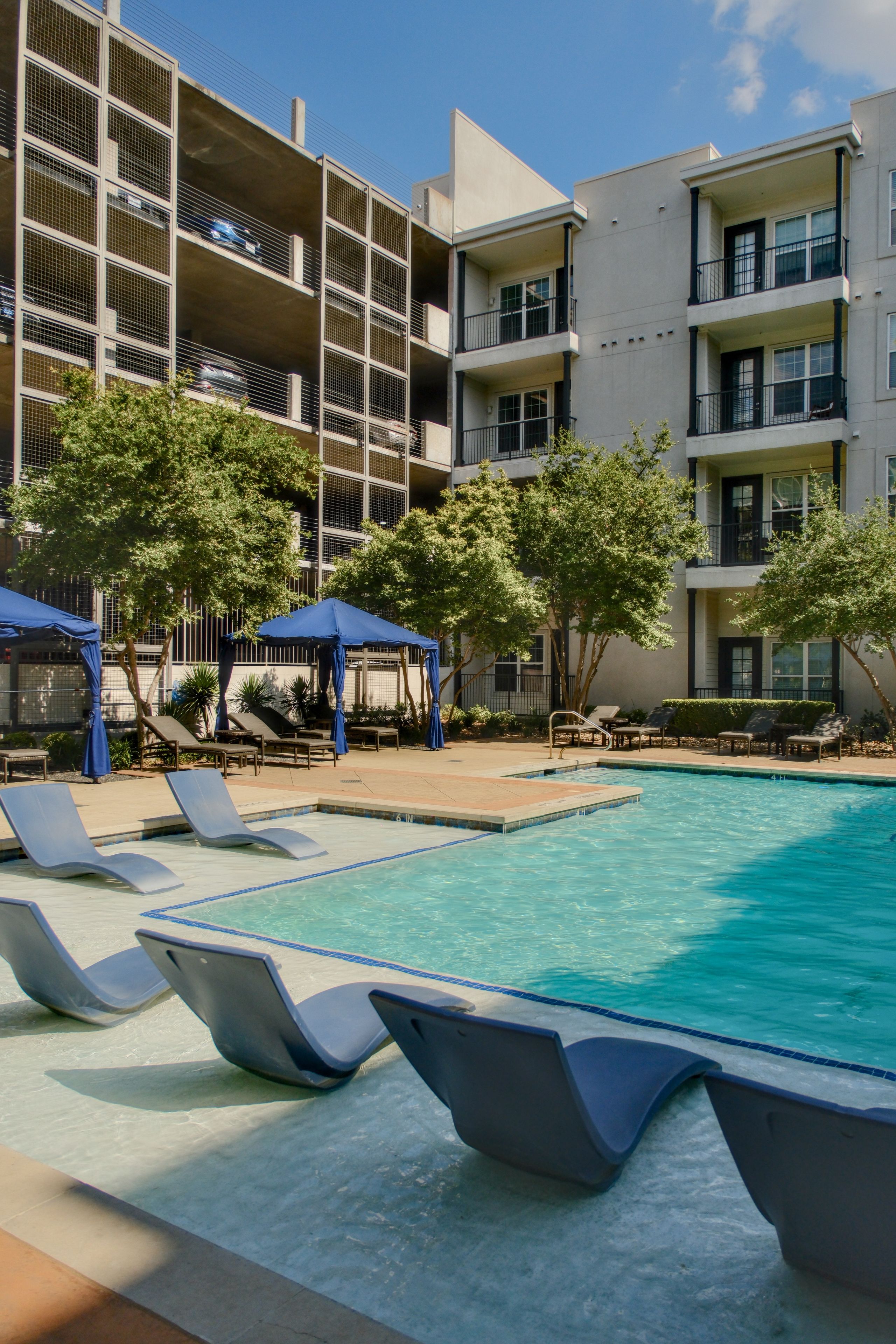 A pool area with lounge chairs and umbrellas, surrounded by multi-story buildings with balconies.