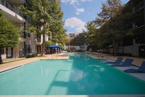 Une piscine entour ée d’arbres et d’immeubles à plusieurs étages, avec des chaises longues à proximité.