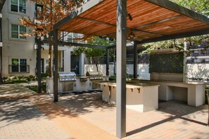 Un espace extérieur aménagé en terrasse, doté d’un coin salon couvert, d’un barbecue et offrant une vue sur un bâtiment en arrière-plan.