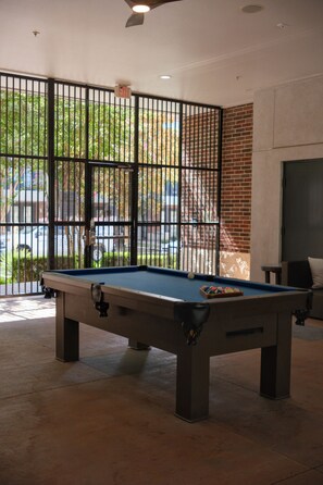 Une table de billard dans une pièce donnant sur l’extérieur, avec vue à travers une grille métallique.