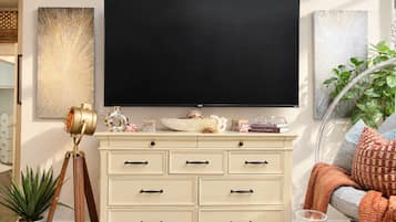 A living room with a large flat-screen TV mounted on the wall, a cream-colored dresser with multiple drawers, a vintage telescope, and a potted plant.