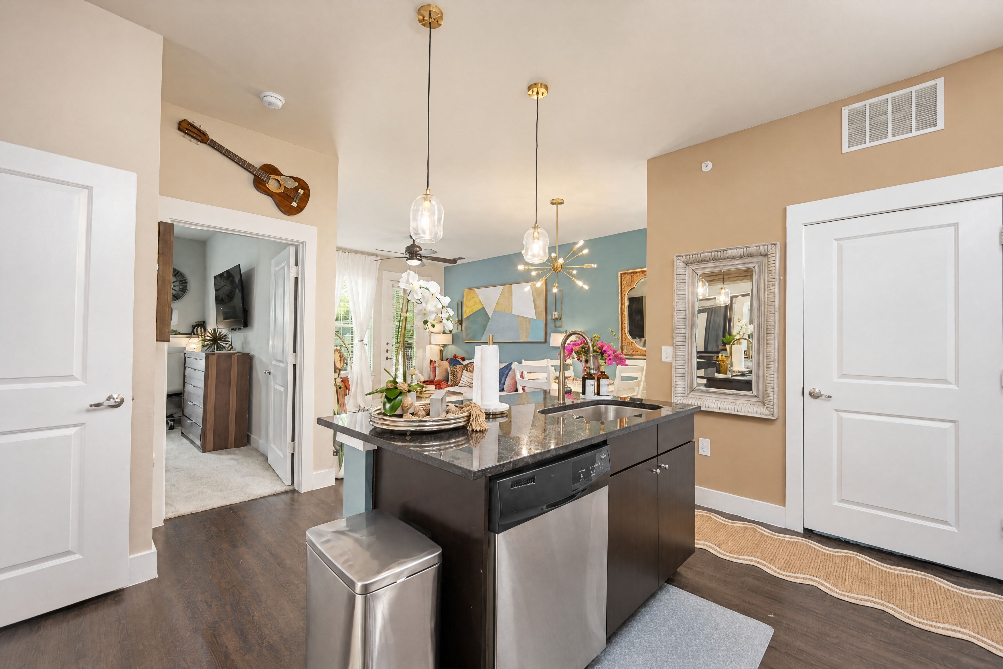 A modern kitchen with a central island, stainless steel appliances, pendant lighting, and a view into the dining area.