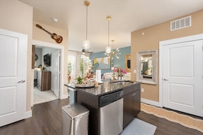A modern kitchen with a central island, stainless steel appliances, pendant lighting, and a view into the dining area. - The Bentley Collection - The Jewel (Dallas)