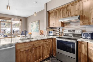 A modern kitchen with wooden cabinets, stainless steel appliances, and a large island with a sink. - Kicking Horse 3BR MTN Retreat Ski-in/out+Hot tub (Golden)