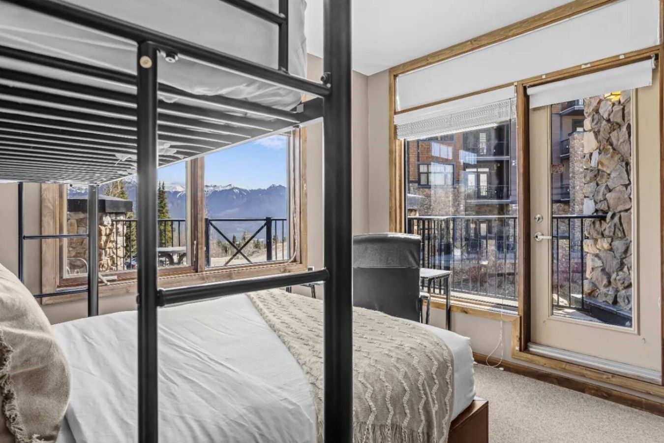 A room with a bunk bed, a view of mountains, a balcony with a railing, and a stone wall.