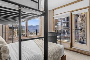 A room with a bunk bed, a view of mountains, a balcony with a railing, and a stone wall. - Kicking Horse 3BR MTN Retreat Ski-in/out+Hot tub (Golden)