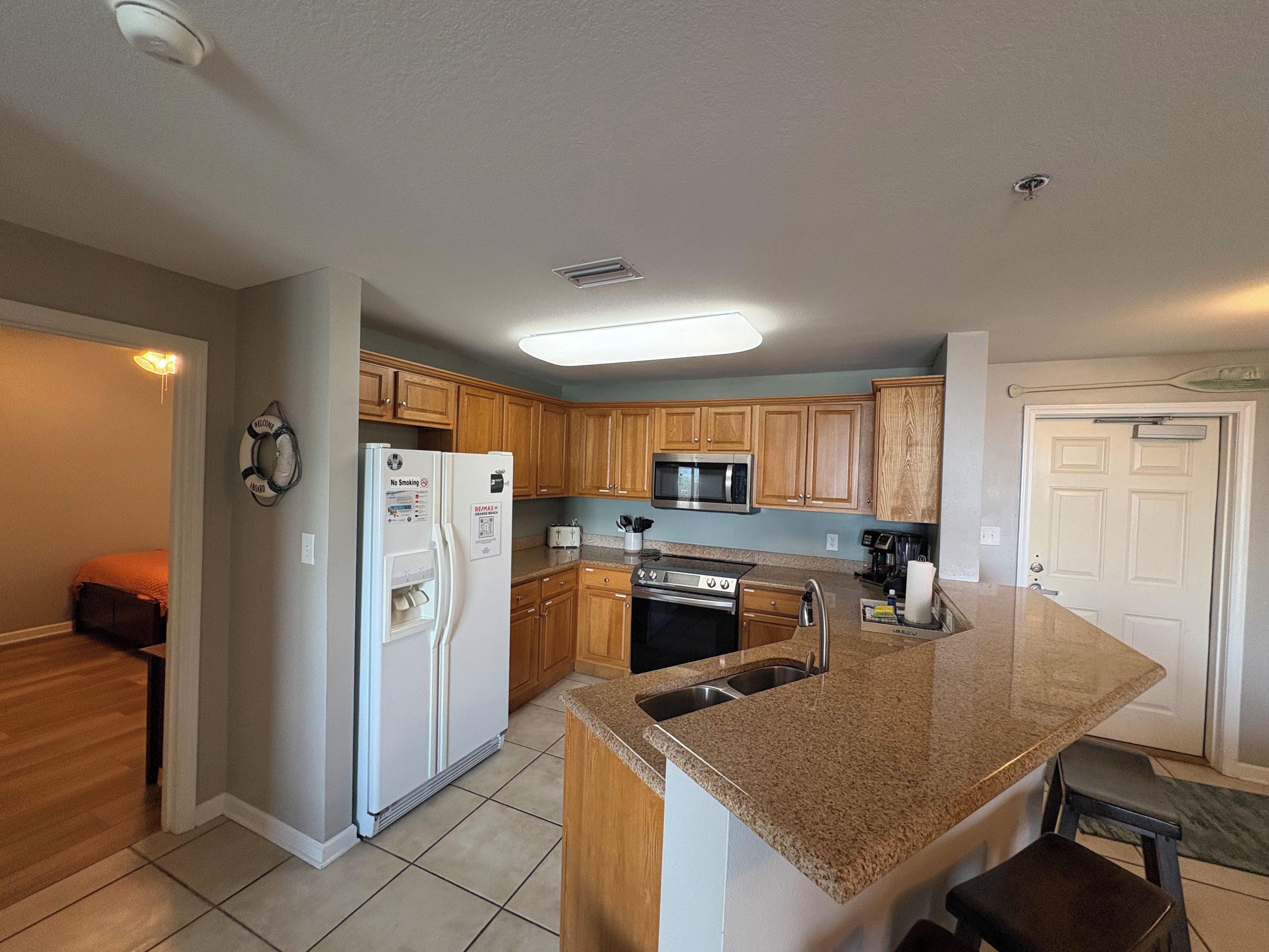 A kitchen with wooden cabinets, a stainless steel refrigerator, a microwave, and a granite countertop.