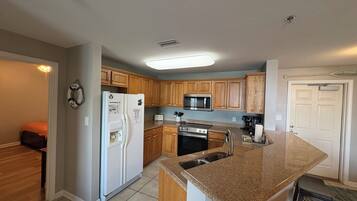 A kitchen with wooden cabinets, a stainless steel refrigerator, a microwave, and a granite countertop.