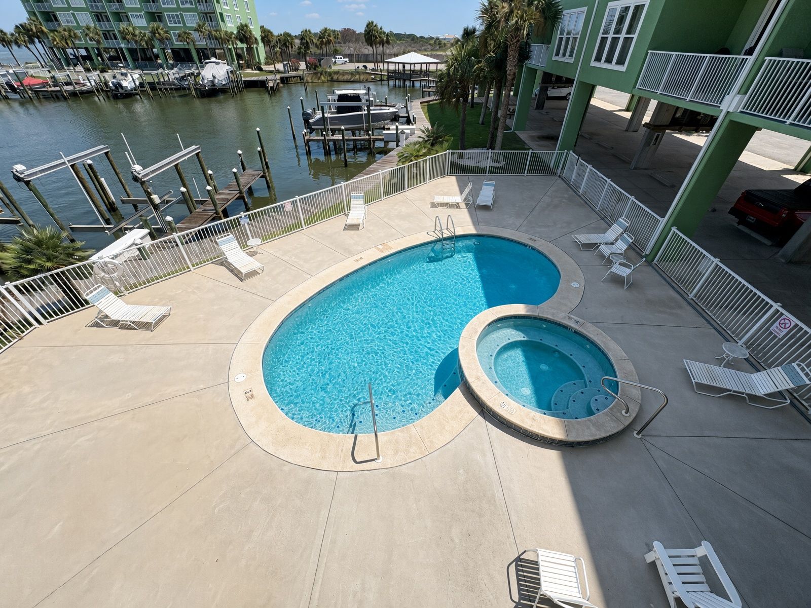 A swimming pool with lounge chairs and a hot tub, surrounded by a deck and a marina view.